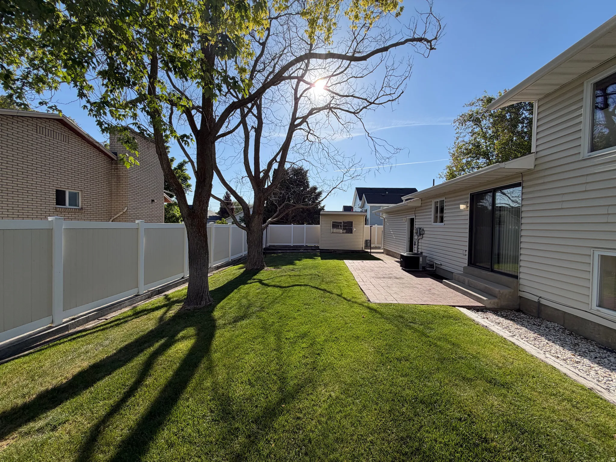 Expansive backyard featuring a manicured lawn, two mature trees, and a privacy fence