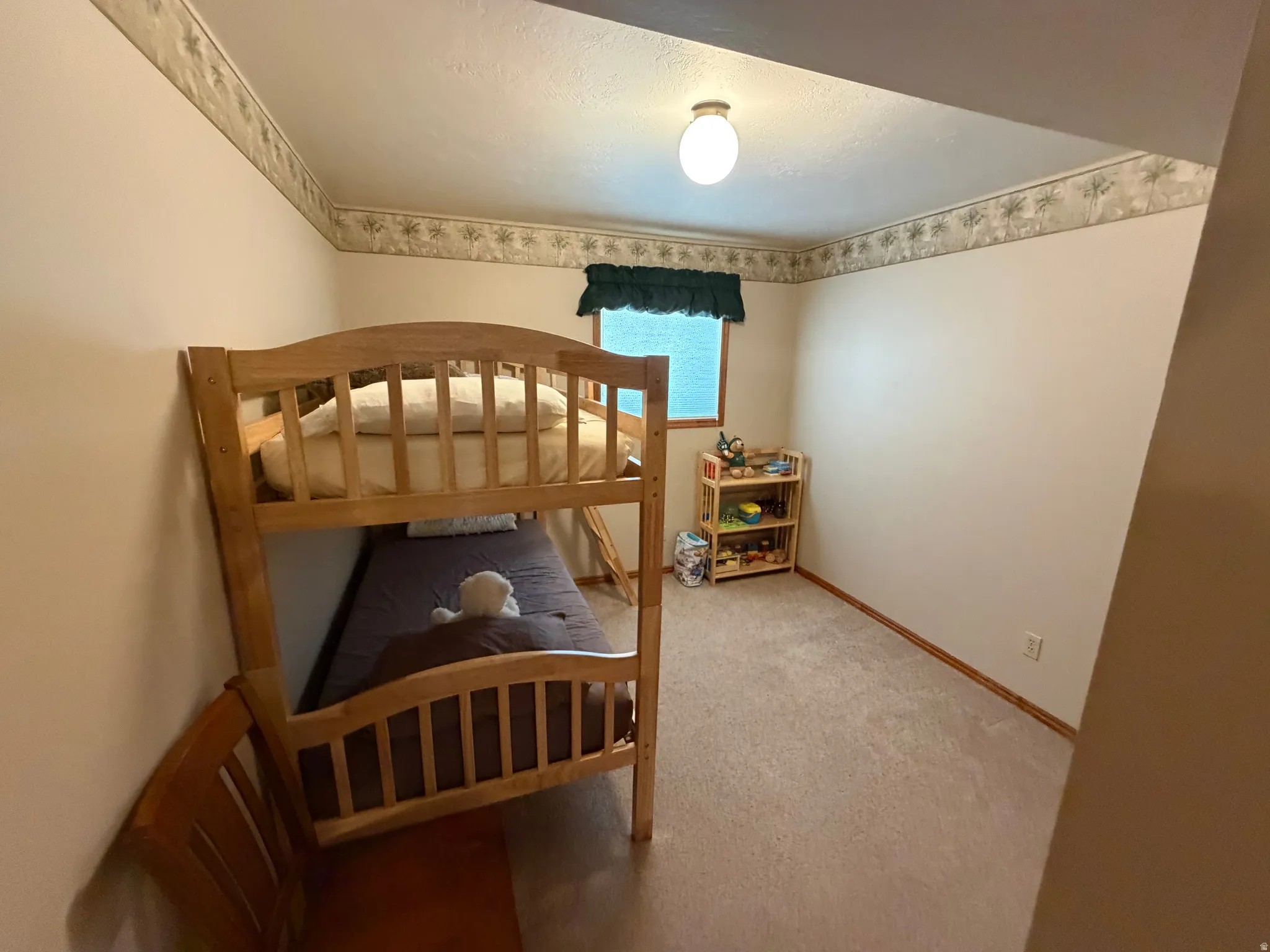 Neutral wall tones with a decorative border, light-colored carpet flooring, and a single window with wood trim
