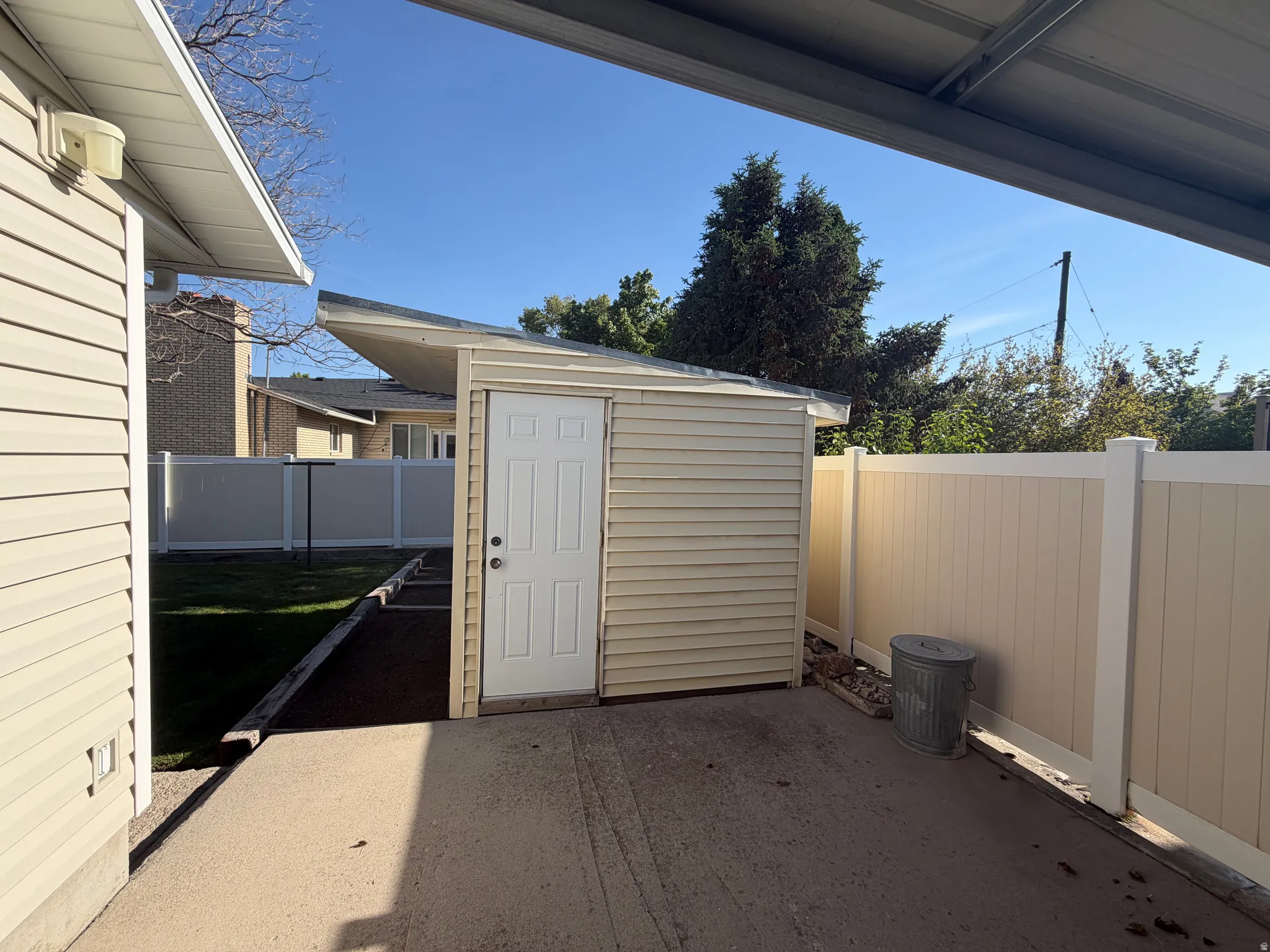 Outdoor storage shed with vinyl siding, a white paneled door, and a sloped roof, situated on a concrete pad