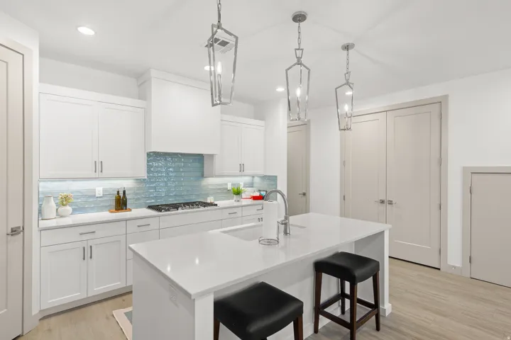 Contemporary kitchen featuring white shaker cabinetry, an expansive center island with seating, a gas range, a unique blue glass tile backsplash, and three geometric pendant lights