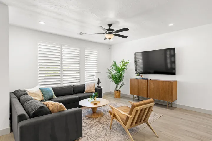 Bright living space featuring multiple windows with plantation shutters, recessed lighting, and a ceiling fan with integrated lighting