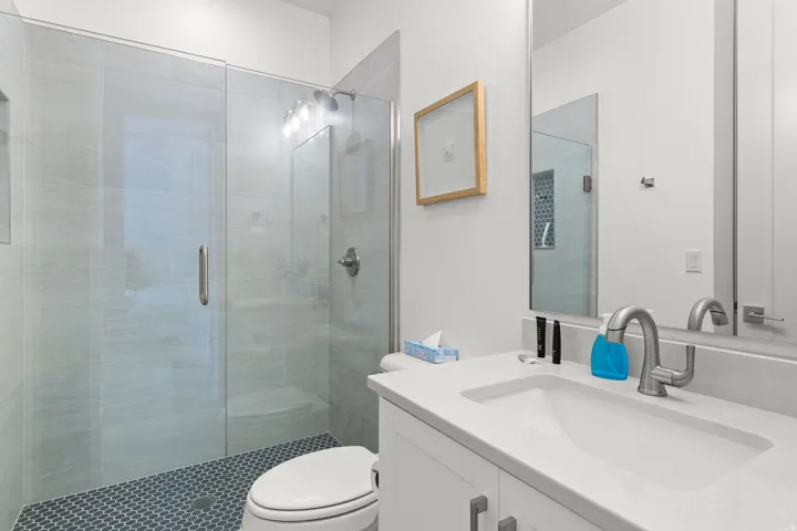 Bathroom featuring a walk-in shower with glass enclosure, light gray wall tile, and dark penny tile flooring