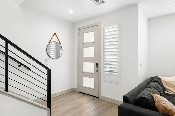 Entryway featuring a modern light-colored door with frosted glass panels, plantation shutters, recessed lighting, and wood-finish flooring