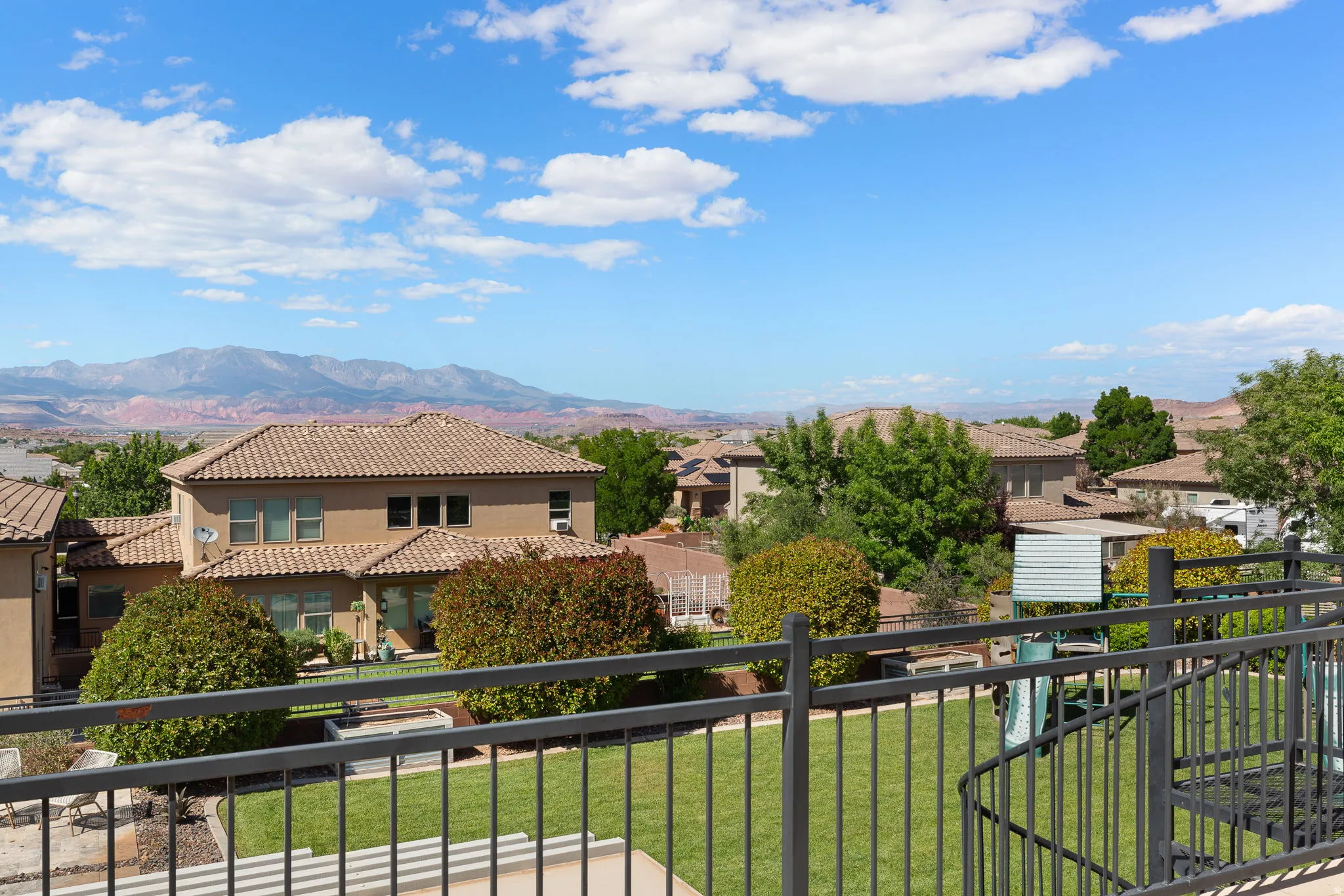Expansive outdoor space featuring a manicured lawn, established landscaping, and a wrought iron railing