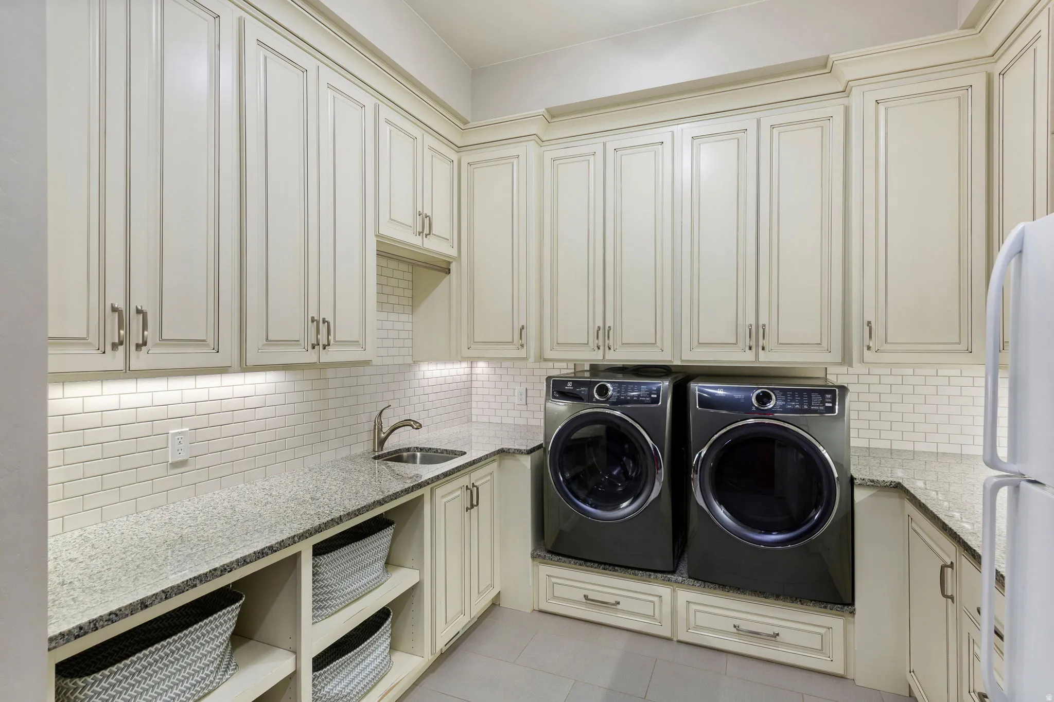 Laundry room featuring extensive custom cabinetry, light-toned granite countertops, a white subway tile backsplash, and an undermount sink