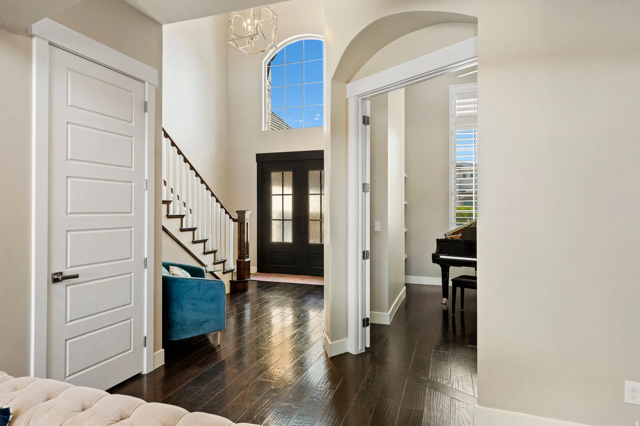 Grand entryway featuring dark wood-finish flooring, a contemporary chandelier, and a prominent arched window