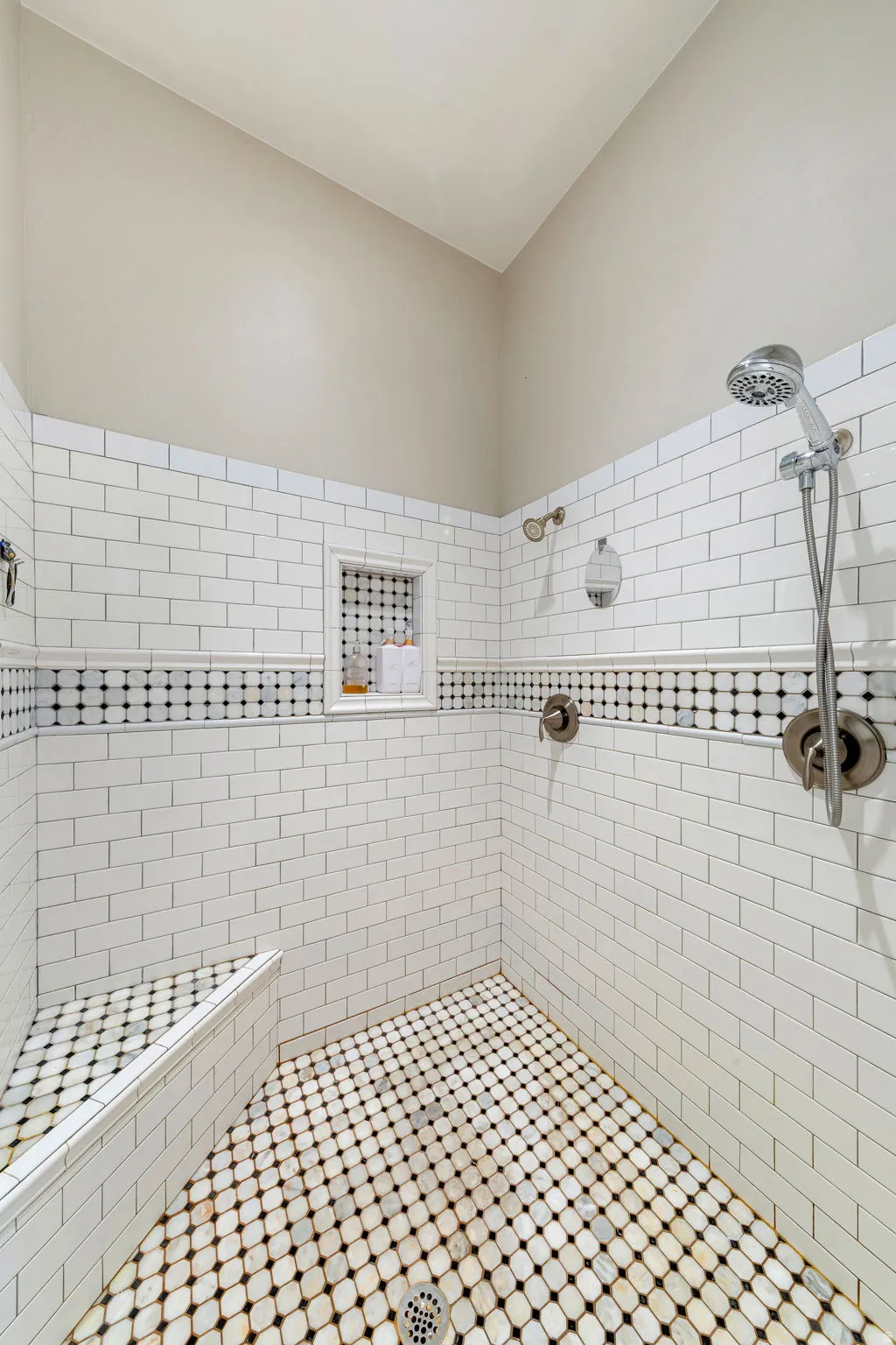 Walk-in shower featuring white subway tile, a decorative black and white mosaic accent band, and an integrated shower bench
