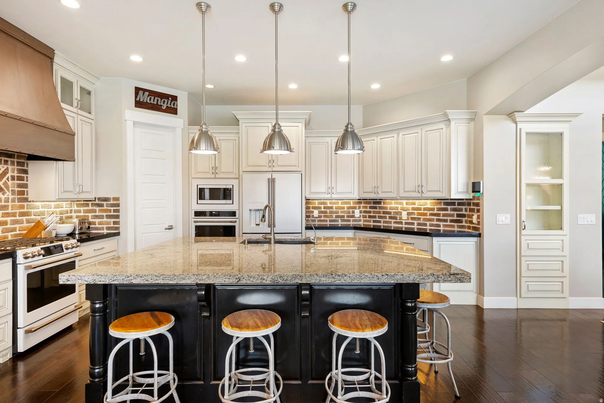 Spacious kitchen featuring a large island with a stone-finish countertop, white cabinetry, a brick-style backsplash, stainless steel appliances, and dark wood-finish flooring