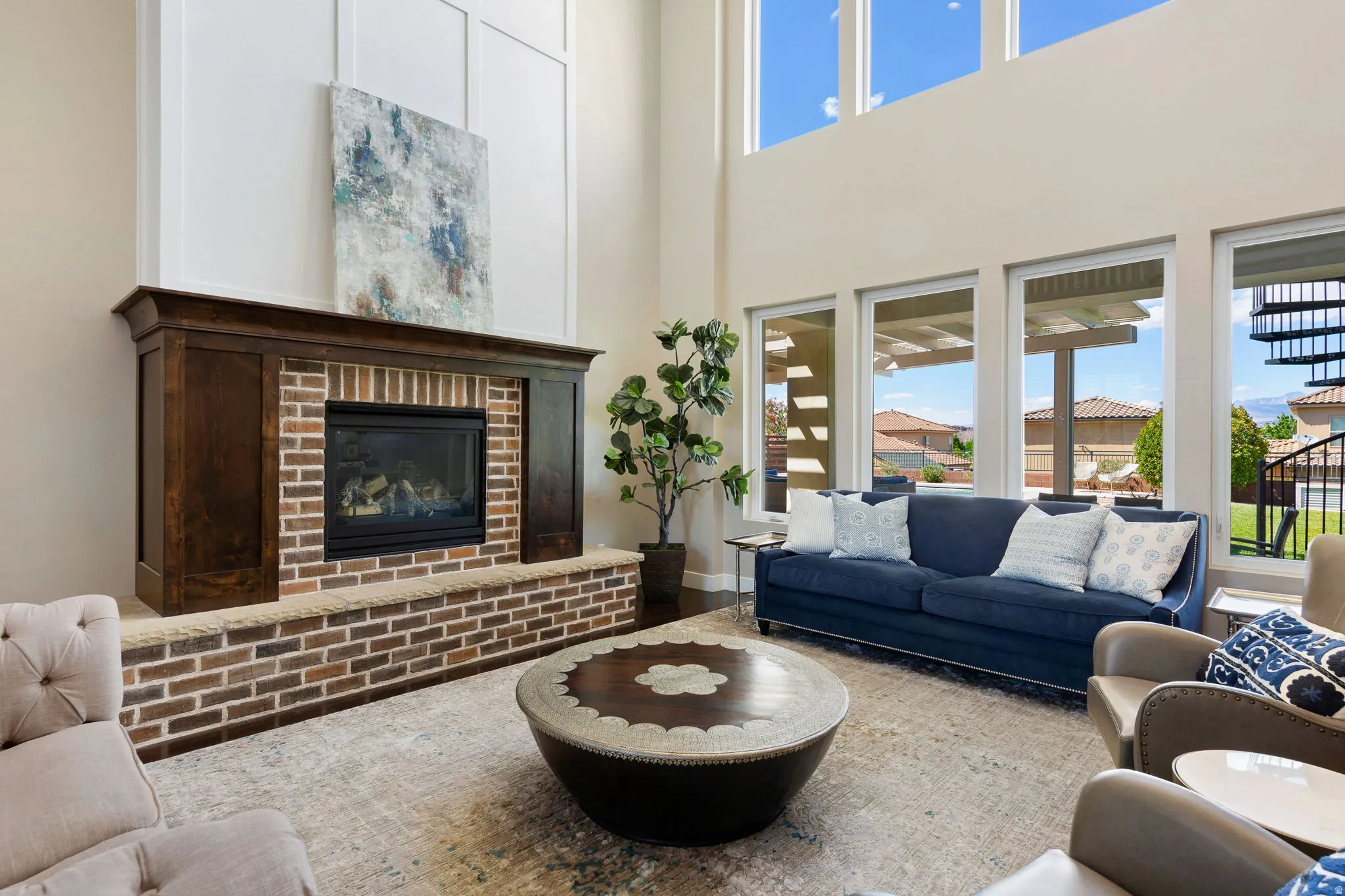 Spacious living area featuring a prominent brick fireplace with a dark wood mantle, soaring ceilings, and expansive windows