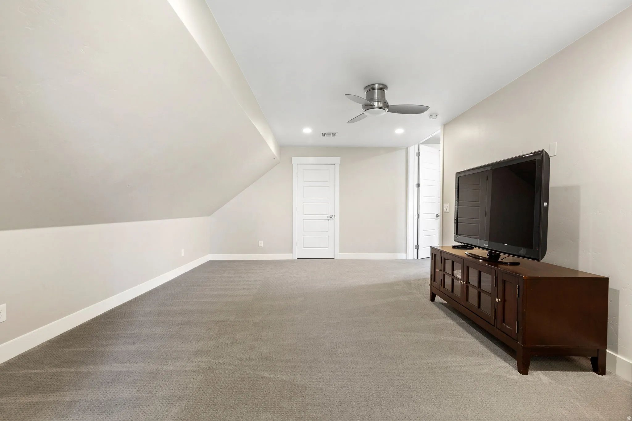 Spacious carpeted room featuring a sloped ceiling, recessed lighting, and a ceiling fan