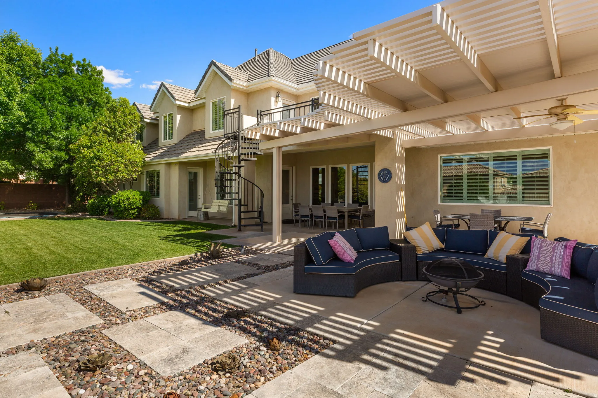 Expansive patio featuring a louvered pergola, outdoor ceiling fan, and decorative stone tile with river rock accents