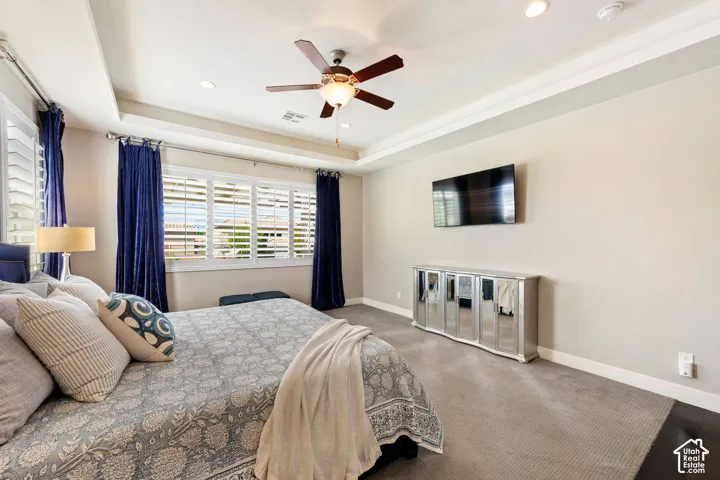 Spacious bedroom featuring neutral wall tones, plush carpeting, and a tray ceiling with recessed lighting
