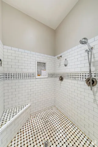 Walk-in shower featuring white subway tile, a decorative black and white mosaic accent band, and an integrated shower bench