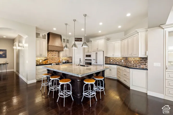 Spacious kitchen featuring a large central island with seating, a brick-patterned backsplash, white cabinetry, dark countertops, and stainless steel appliances