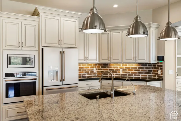 Kitchen featuring a multi-tone granite island with an undermount sink, three industrial-style pendant lights, an integrated microwave and oven, a side-by-side refrigerator, and a brick-patterned backsplash