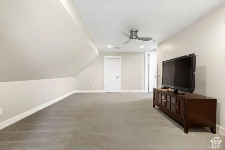 Spacious carpeted room featuring a sloped ceiling, recessed lighting, and a ceiling fan