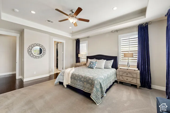 Carpeted bedroom featuring a tray ceiling with recessed lighting and a ceiling fan