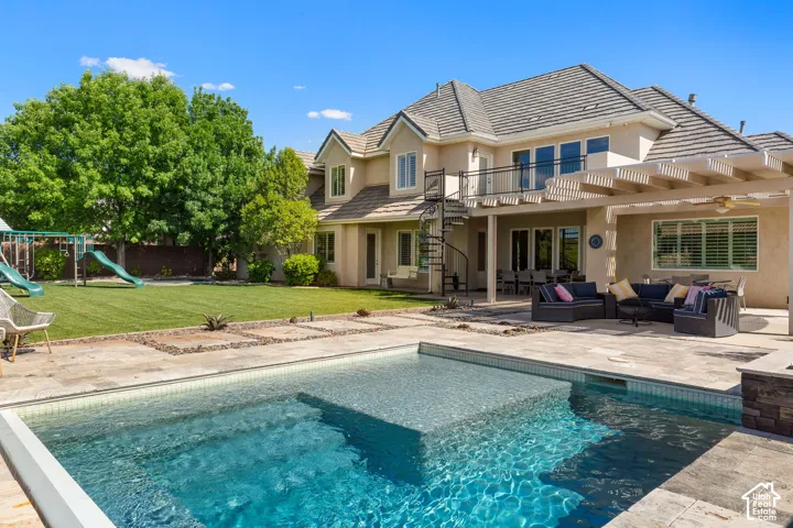 Backyard oasis featuring an in-ground swimming pool with an integrated spa, expansive paver patio, covered outdoor living area with a pergola, spiral staircase access to the upper level, and a large manicured lawn