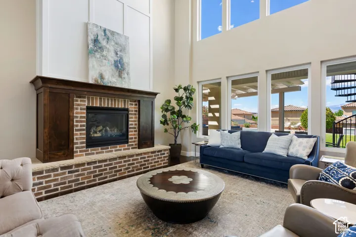 Spacious living area featuring a prominent brick fireplace with a dark wood mantle, soaring ceilings, and expansive windows