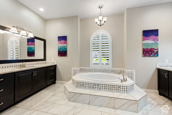 Spacious bathroom featuring a built-in corner soaking tub, arched window with plantation shutters, dual vanity with dark wood cabinetry, white countertops, and tile flooring