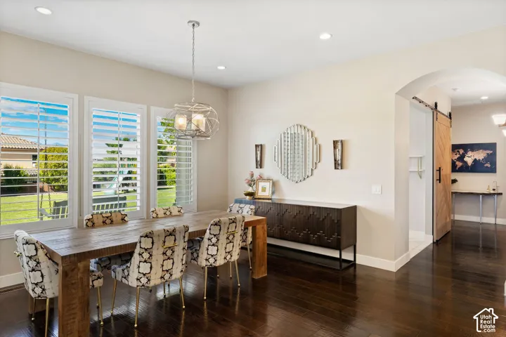 Dining area featuring dark wood-finish flooring, three large windows with white louvered shutters, and a modern geometric pendant light fixture