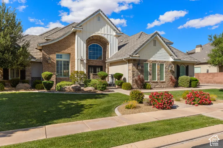 Exterior featuring brick and stone masonry, a multi-gabled roofline with dimensional shingles, an arched window above double entry doors, and board and batten siding accents