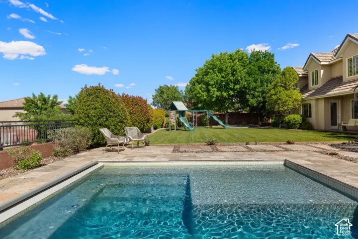 Backyard oasis featuring a swimming pool with integrated tanning ledge, stone paver patio, expansive lawn, and mature landscaping