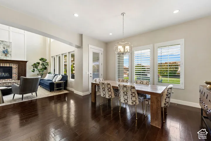 Open-concept dining area with dark wood-finish flooring, a contemporary chandelier, and three large windows featuring plantation shutters