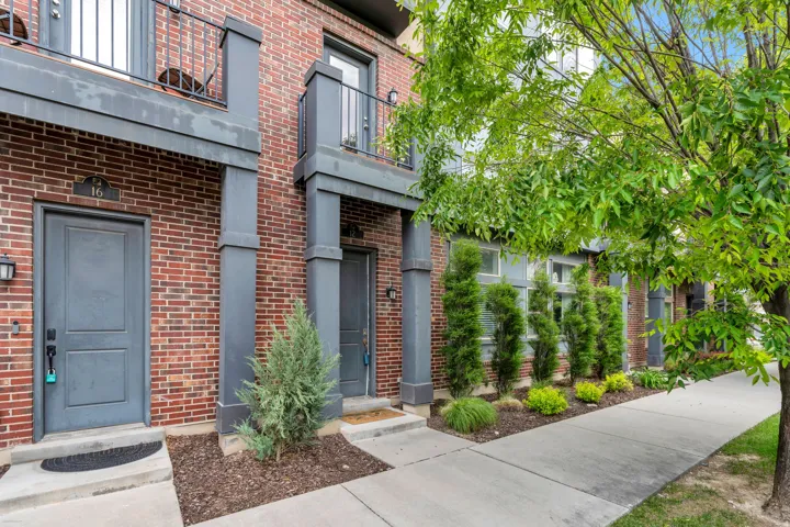 Brick exterior featuring a private entrance, an upper-level balcony with metal railing, and a mature tree providing natural shade