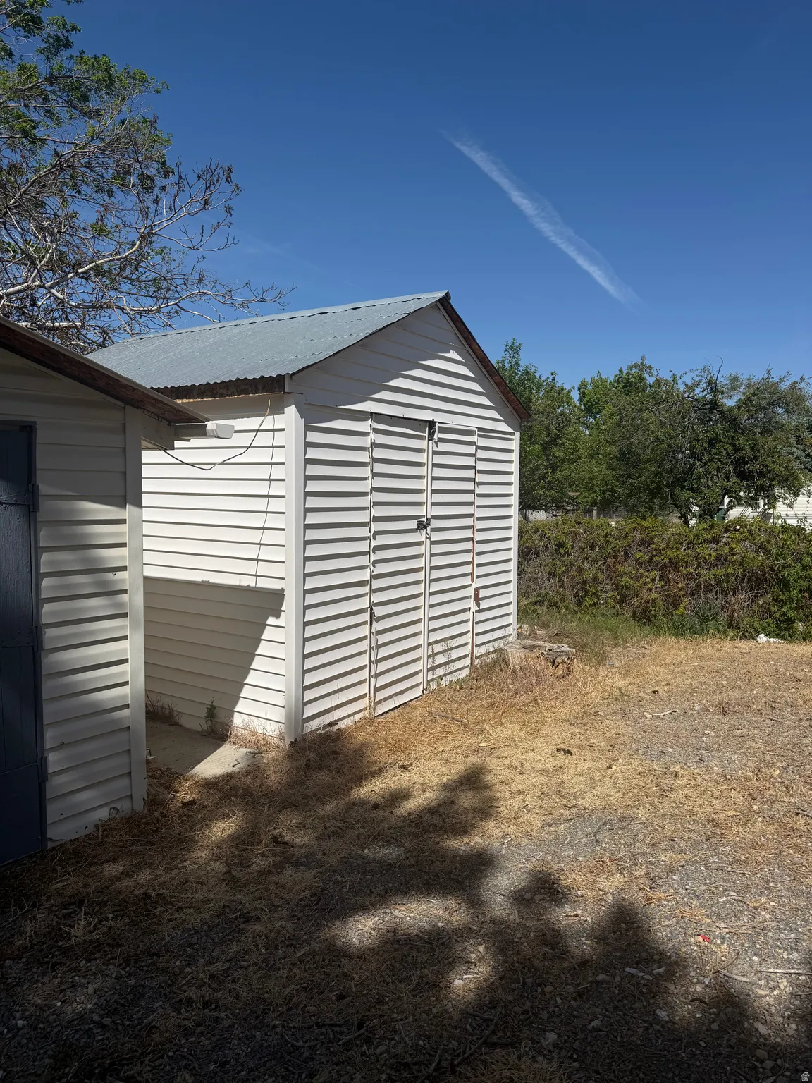 White storage shed featuring horizontal siding and a corrugated metal roof