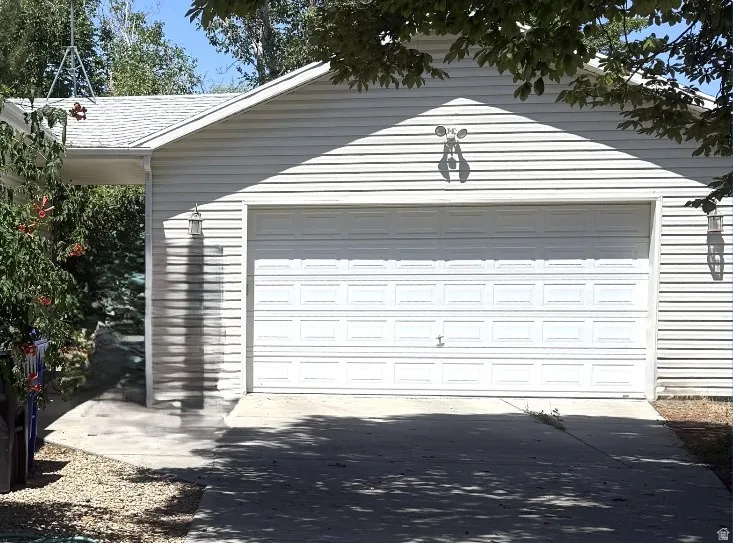 Attached two-car garage  approx. 30x40, featuring panel-style door, white vinyl siding, and exterior lighting fixtures  for appearance and safety motion light & side entry motion light. Garage door opener.