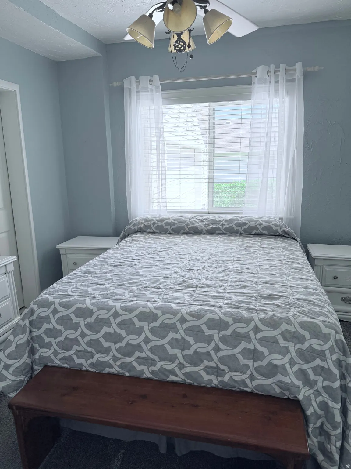 Bedroom featuring a ceiling fan with integrated lighting, window with blinds and sheer curtains, and light blue wall color