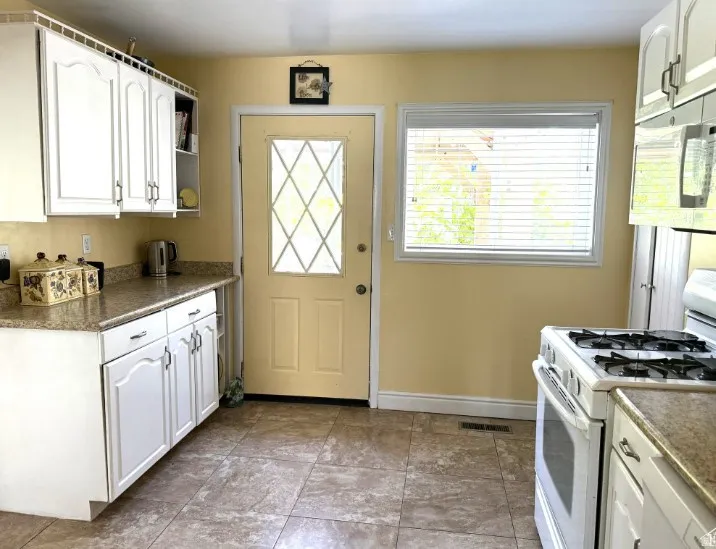 Kitchen featuring tile flooring, white cabinetry, granite-finish countertops, and a gas range. over the stove newer microwave.