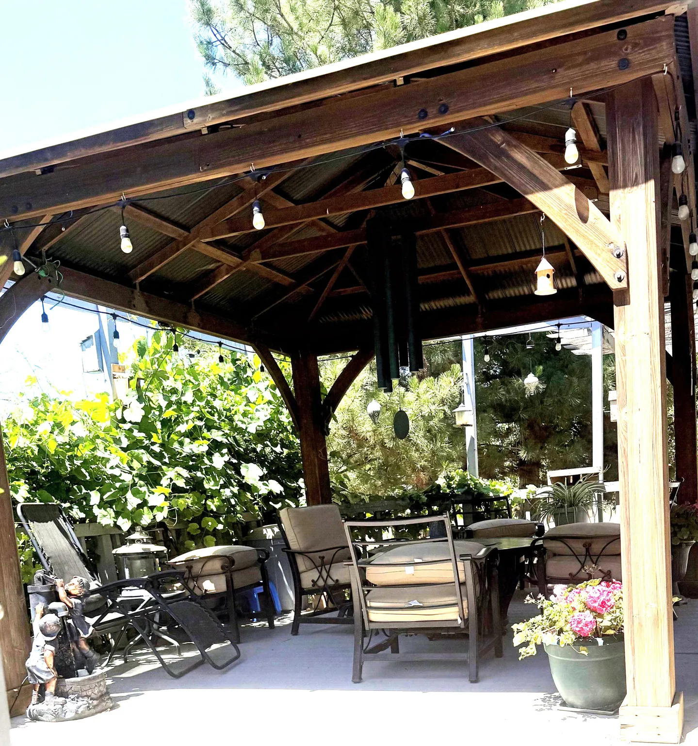 Outdoor gazebo featuring a corrugated metal roof, substantial wood beams, and perimeter string lighting,  Large chime, trex decking outdoor lights.