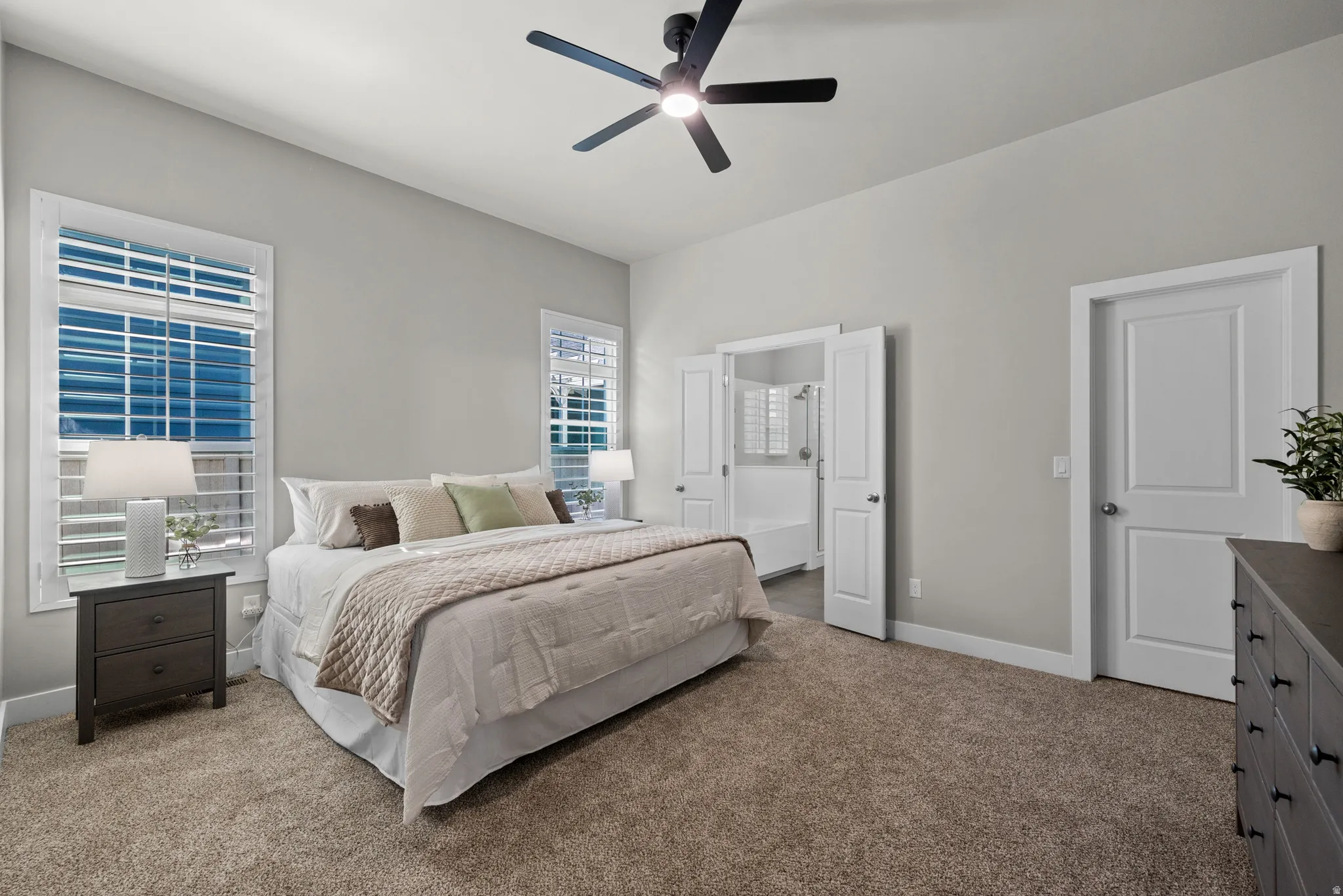 Carpeted room featuring light gray walls, white trim, two windows with plantation shutters, a ceiling fan, and two interior doors