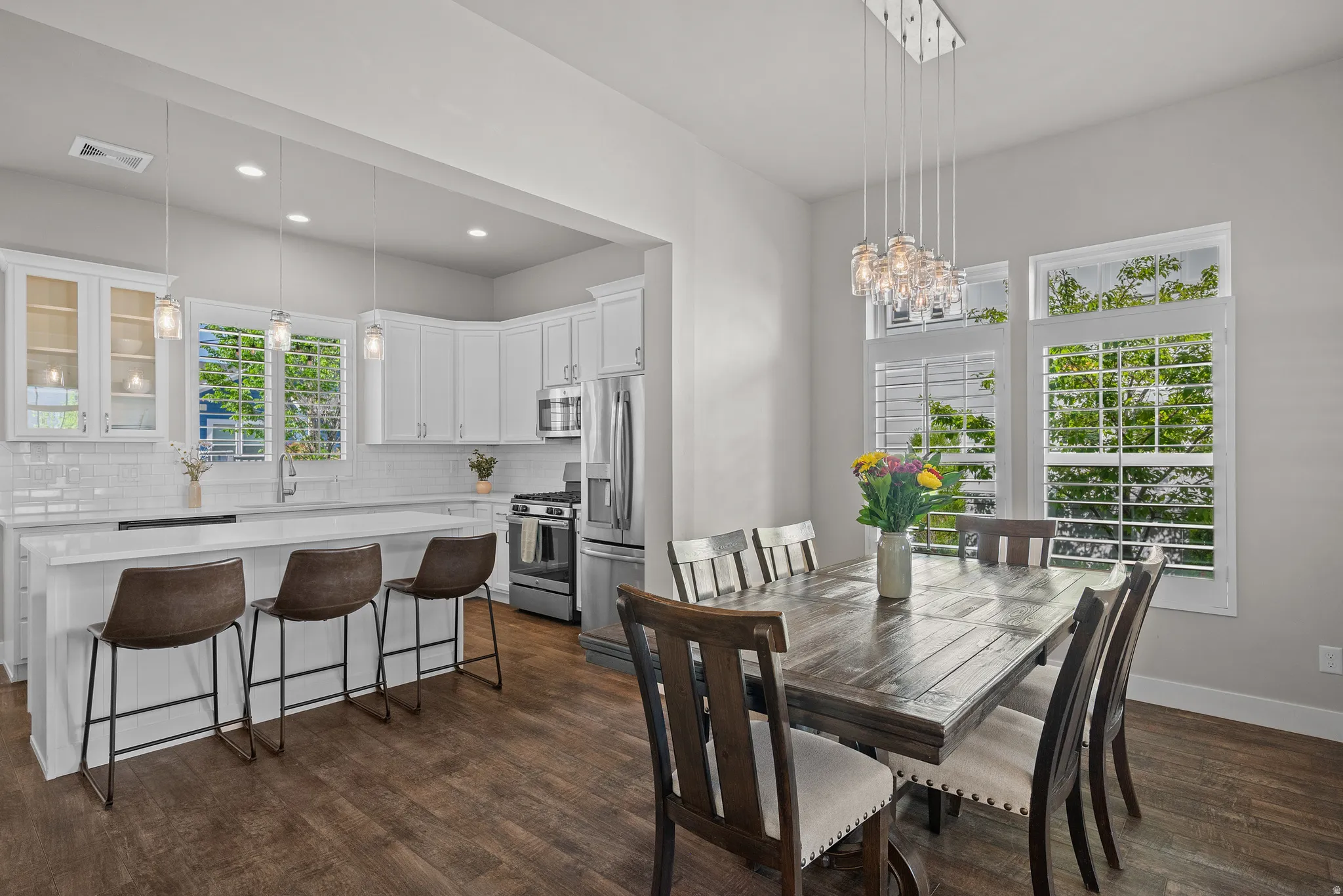 Open-concept dining area and kitchen featuring wood-finish flooring, white cabinetry, stainless steel appliances, and a white subway tile backsplash