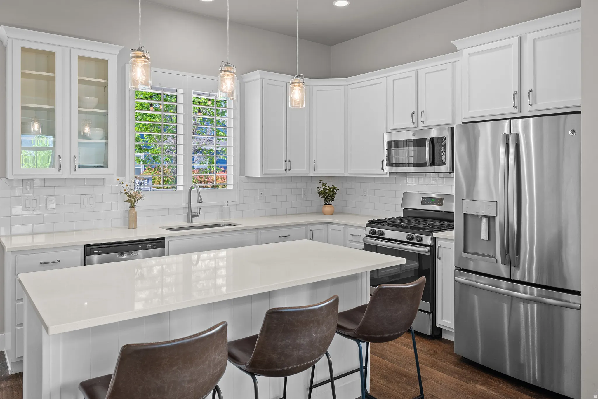 Kitchen featuring white shaker cabinetry, stainless steel appliances, a white subway tile backsplash, and quartz countertops, including a central island with paneling