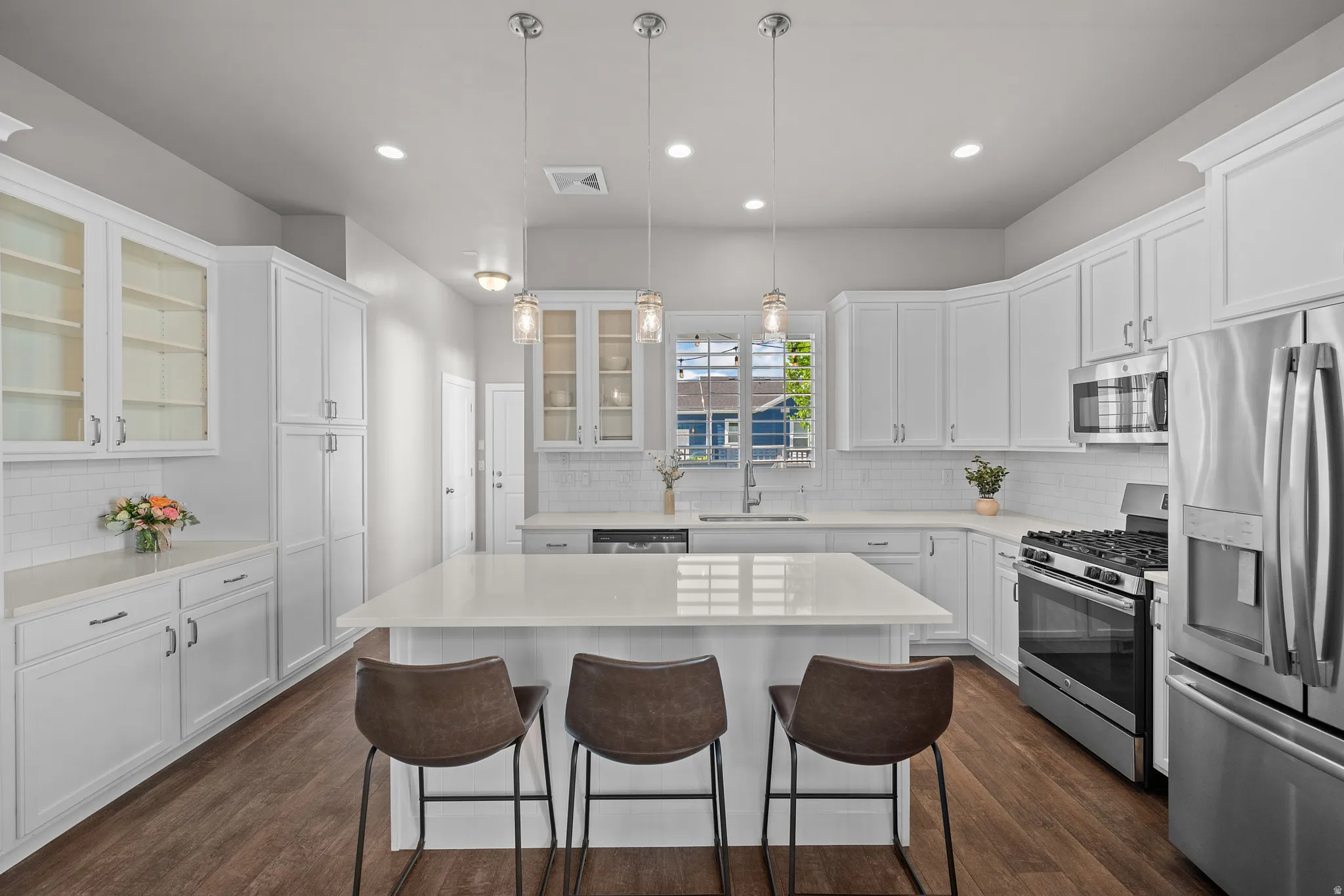 Modern kitchen featuring a large central island with seating, white shaker-style cabinetry, stainless steel appliances, white subway tile backsplash, and wood-finish flooring