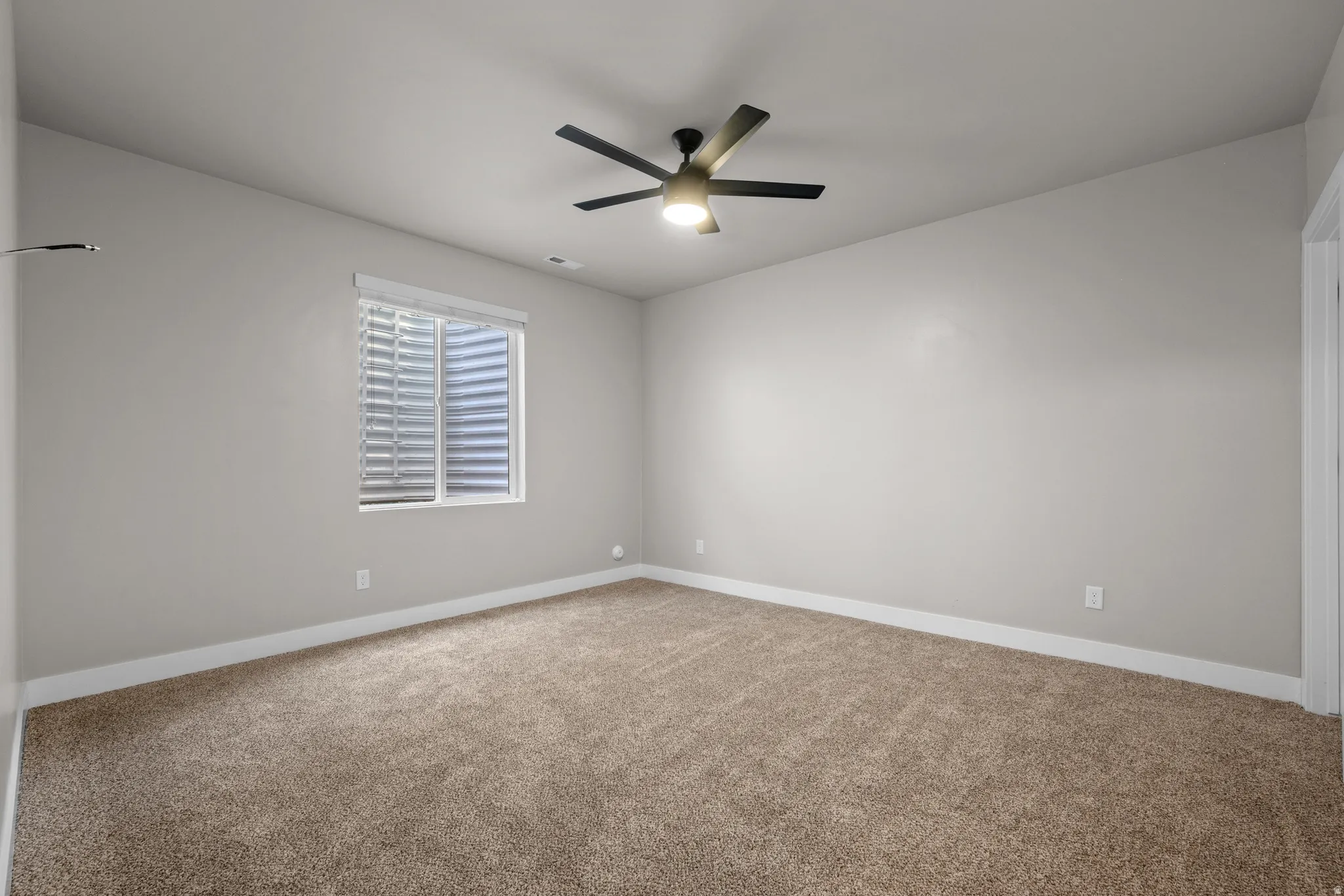 Carpeted room featuring a ceiling fan with integrated lighting, a window with blinds, light gray walls, and white baseboards