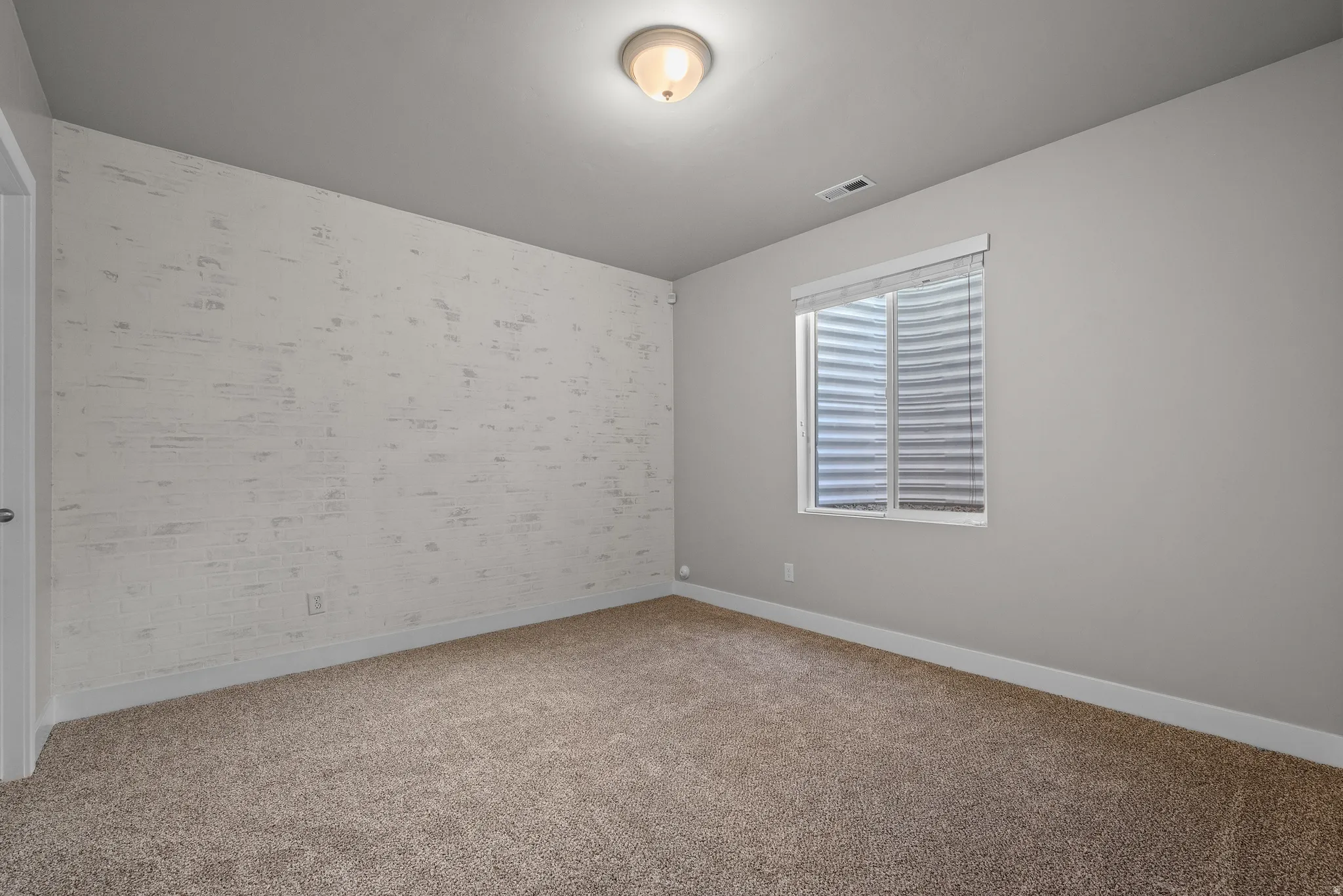 Carpeted room featuring a textured accent wall and a window with horizontal blinds
