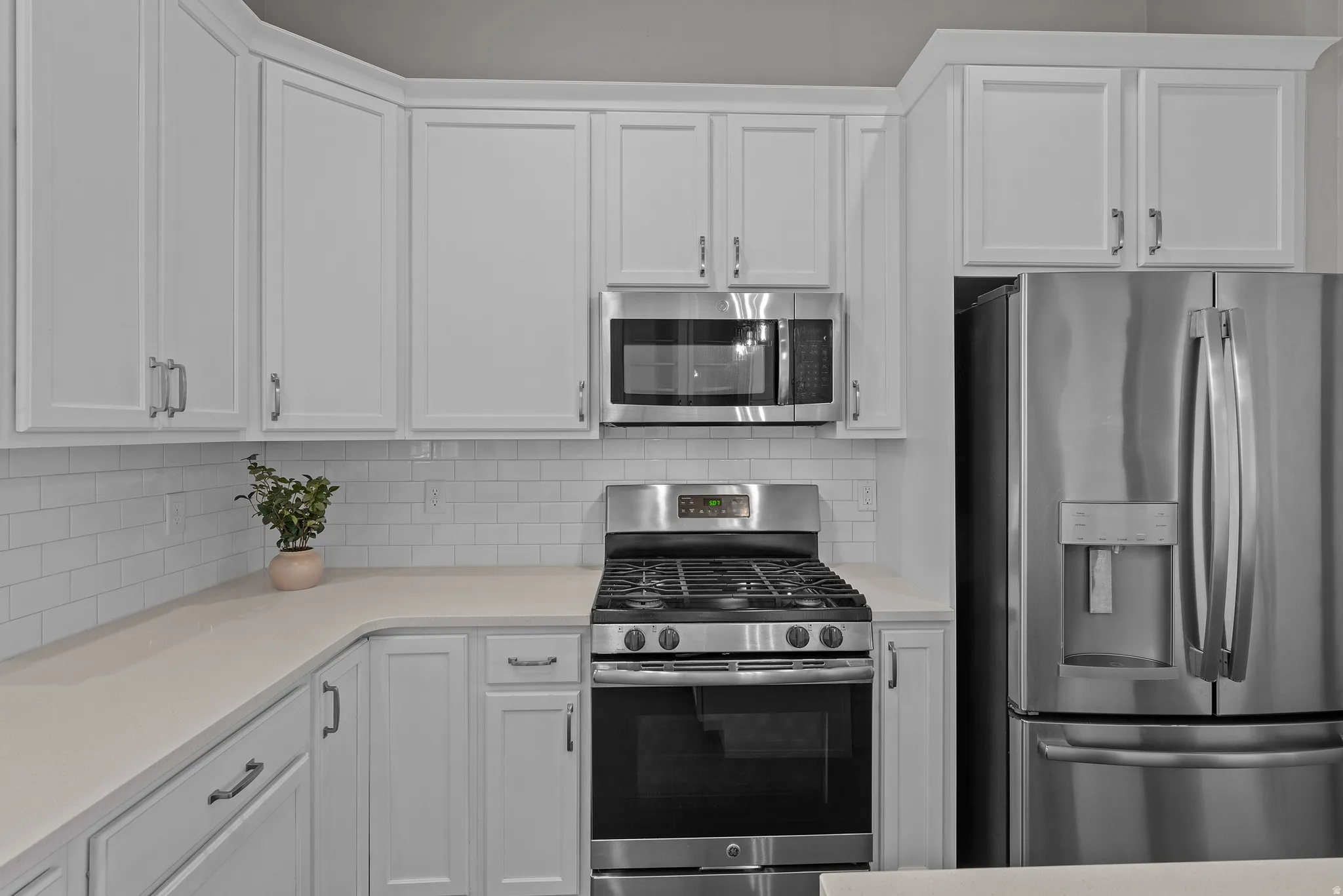 Kitchen featuring white cabinetry, light-toned countertops, white subway tile backsplash, and stainless steel appliances including a gas range, microwave, and refrigerator