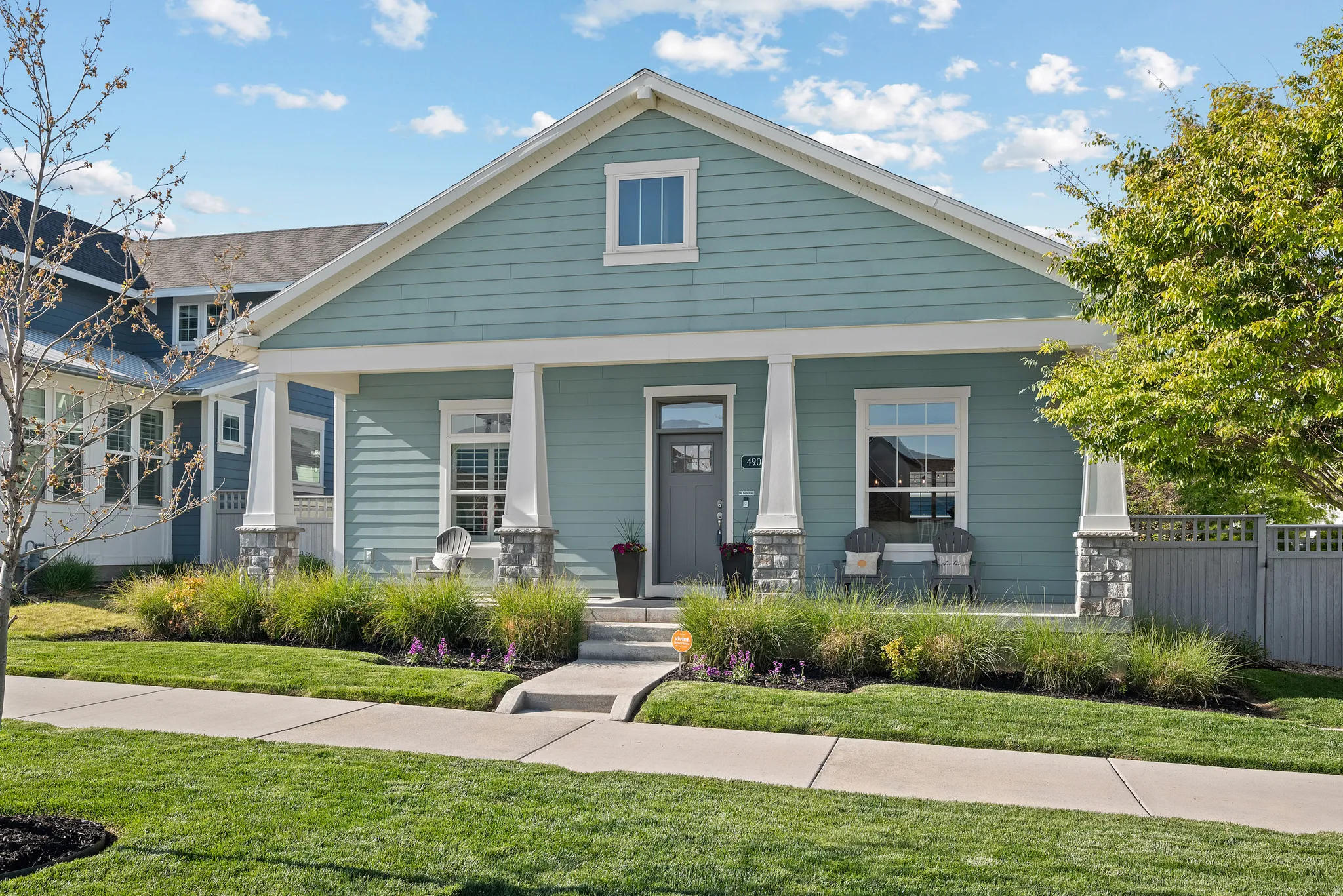 Turquoise siding exterior with white trim, a covered front porch, stone-wrapped columns, a grey front door, and a manicured lawn with established landscaping