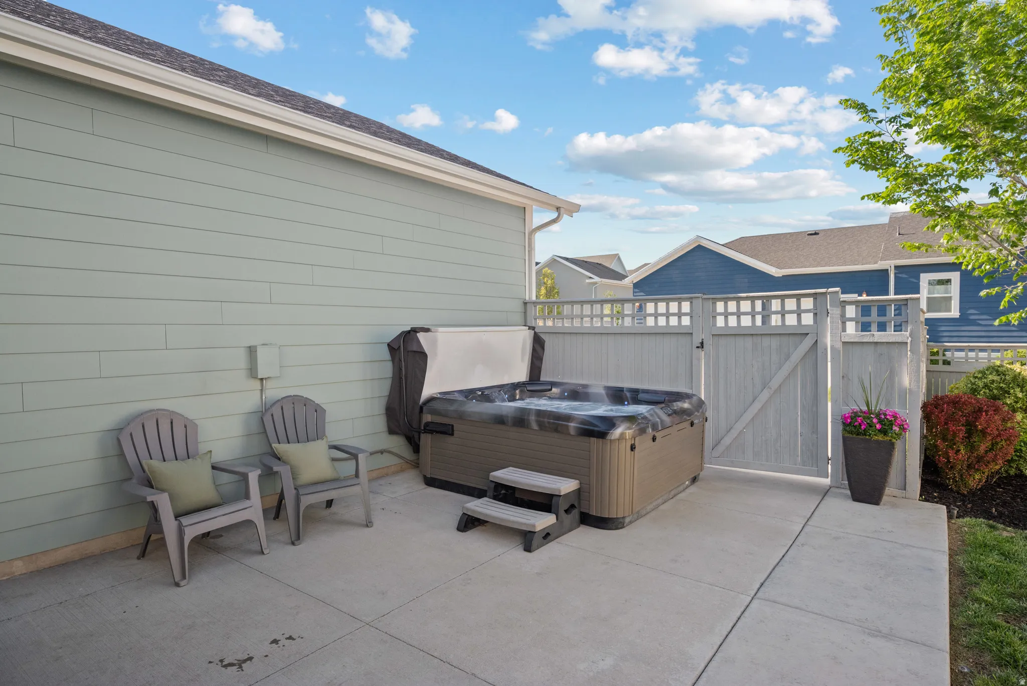 Private patio featuring a built-in hot tub, concrete slab, slat-style fencing, and green landscaping