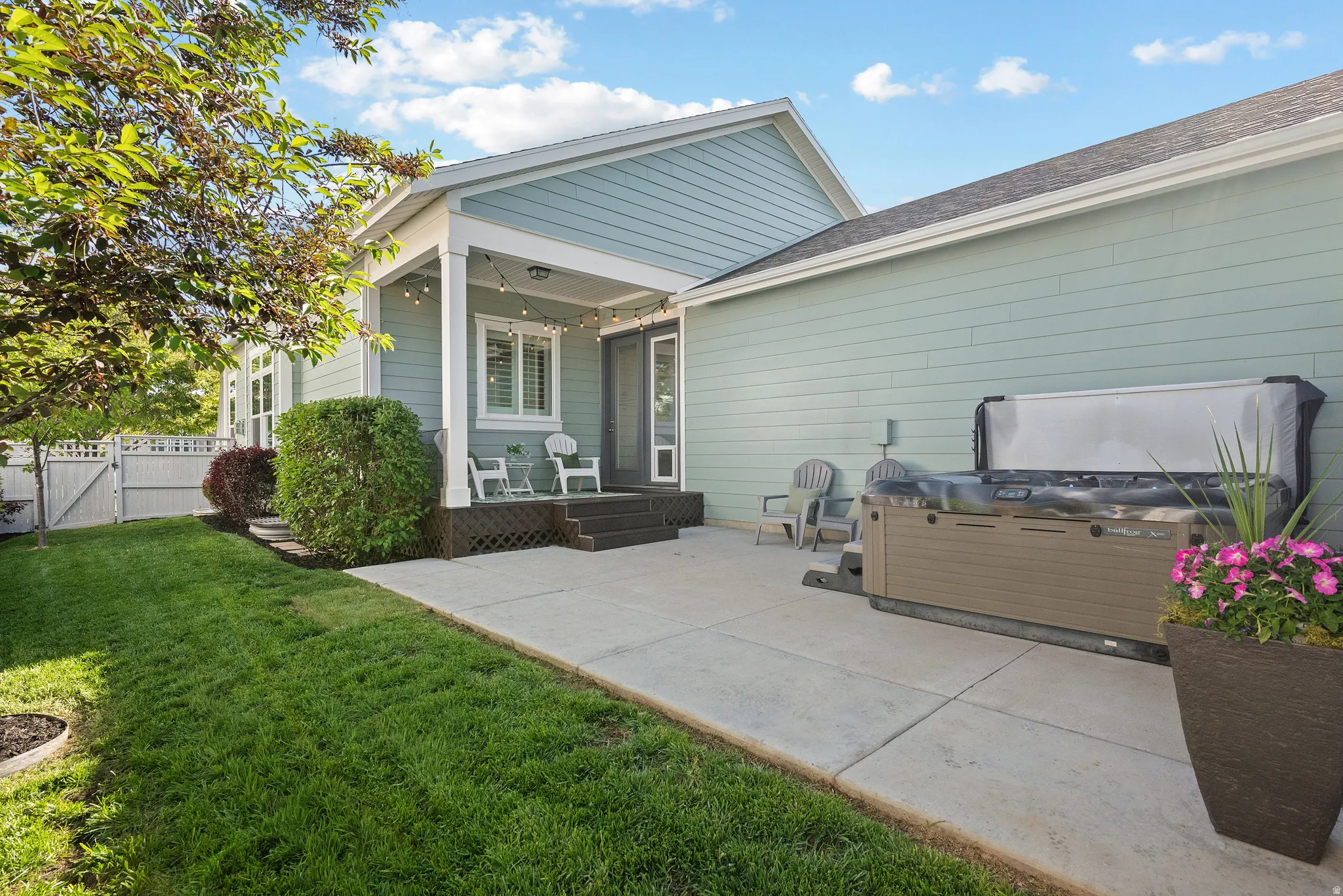Expansive concrete patio area featuring a hot tub with cover, green lawn, and a light blue siding exterior