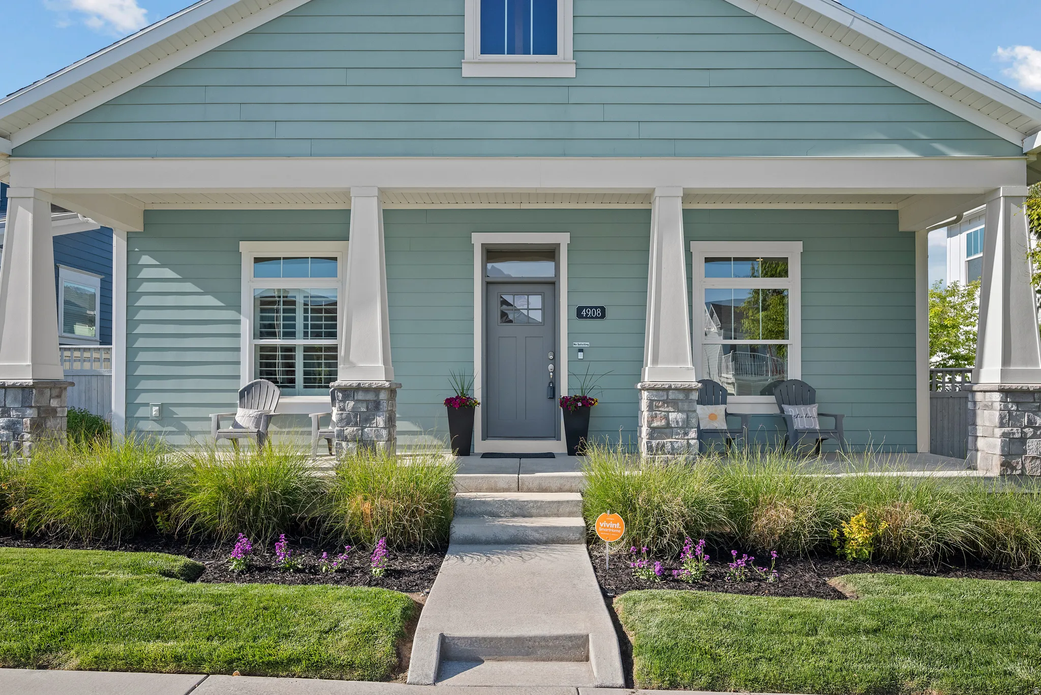 Front exterior with a covered porch featuring stone-clad pillars, light blue horizontal siding, and white trim accents