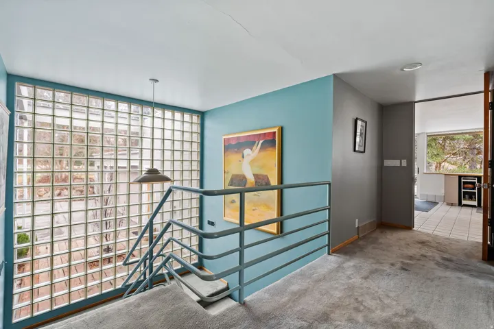 Staircase with glass block wall, metal railing, and carpeted treads