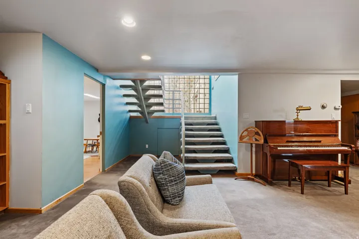 Carpeted living area featuring recessed lighting, a sliding door opening to wood-finish flooring, a staircase with glass block accents, and light blue wall details