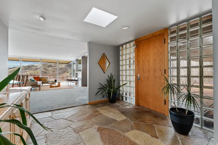 Foyer featuring flagstone flooring, a skylight, a wood-finish entry door, and glass block wall elements