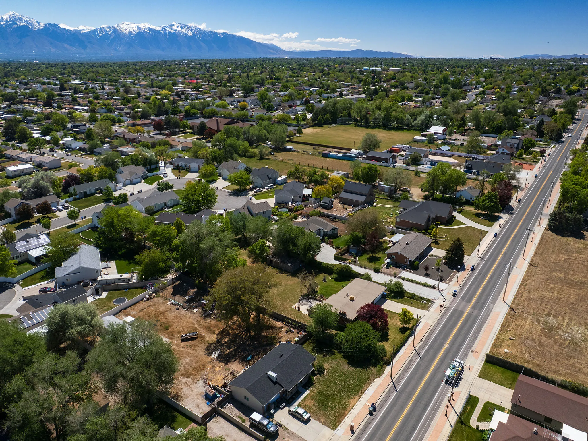 Expansive aerial view showcasing a developed neighborhood with mature trees and a clear mountain backdrop