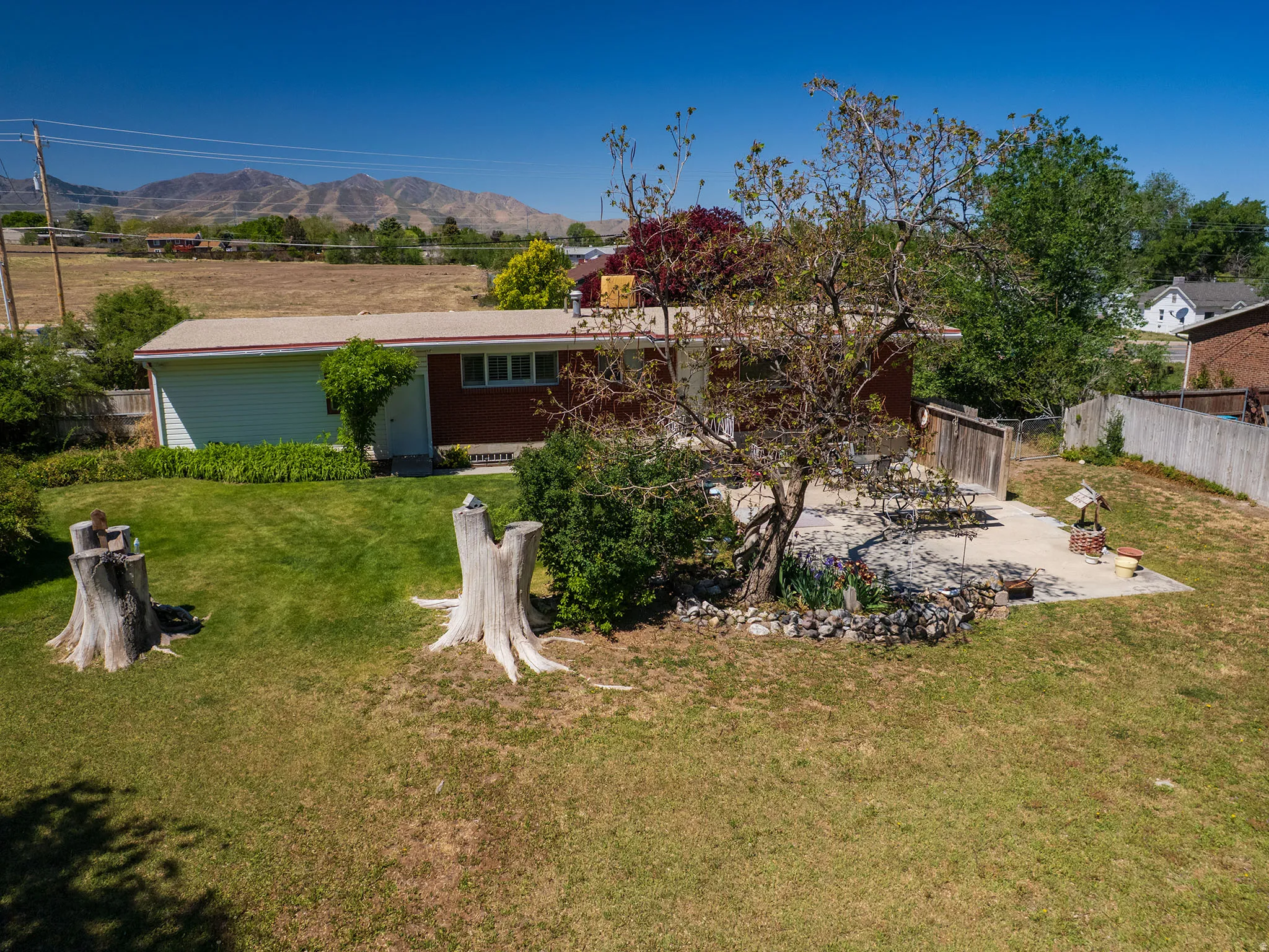 Expansive backyard featuring a large concrete patio, mature trees, manicured lawn, and mountain scenery
